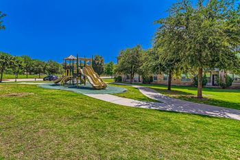 A playground in a park with green grass and trees